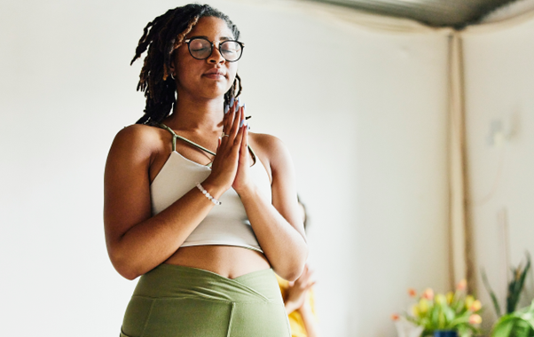 A woman in yoga attire stands in a room, embodying strength and focus as she prepares for her exercise routine
