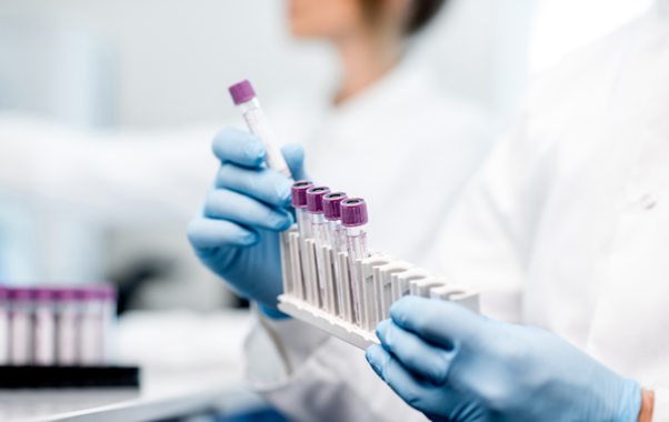 A laboratory professional in a white coat presents a tube of blood, emphasizing the importance of clinical analysis