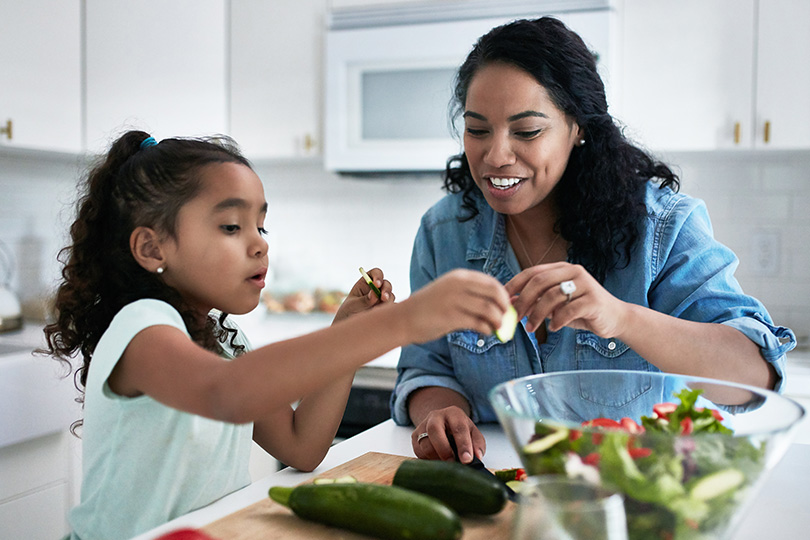 A woman and a child chop vegetables together in a kitchen, promoting heart-healthy eating habits.