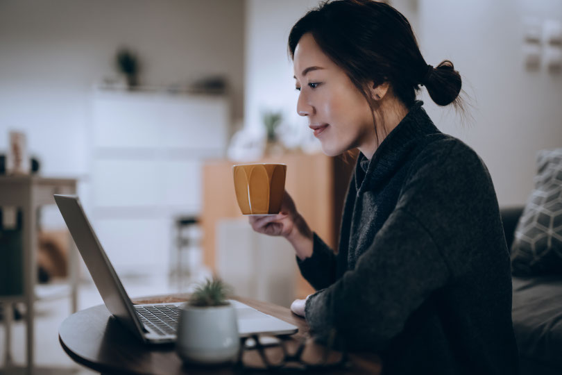 Woman sips coffee at desk.