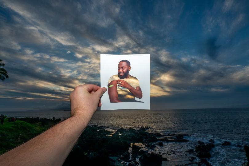 Individual holding a photo of a man at the beach, showcasing a serene moment by the water's edge.