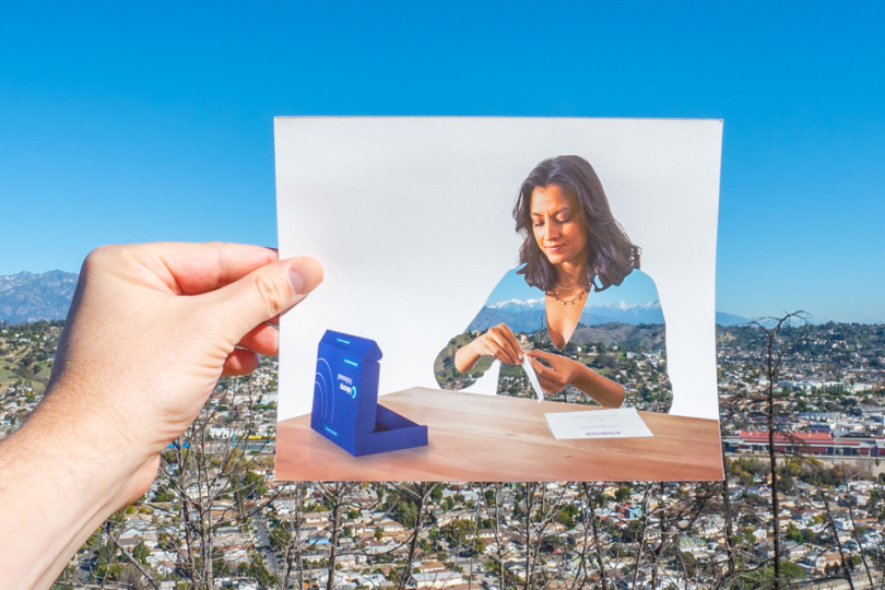 A hand displays a photo of a woman unboxing the kit items, set against a bustling cityscape in the background.