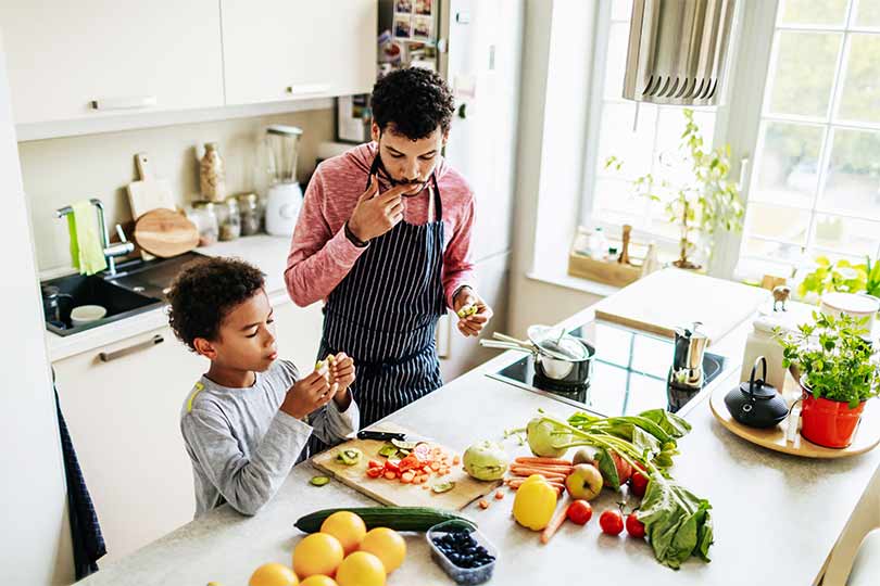 A father and son cooking together in the kitchen, practicing healthy habits that can help maintain healthy adiponectin and leptin hormone levels to support cardiovascular health.