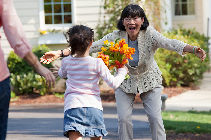 A woman stands with flowers while a little girl runs energetically, symbolizing the beauty of spring and outdoor activities.