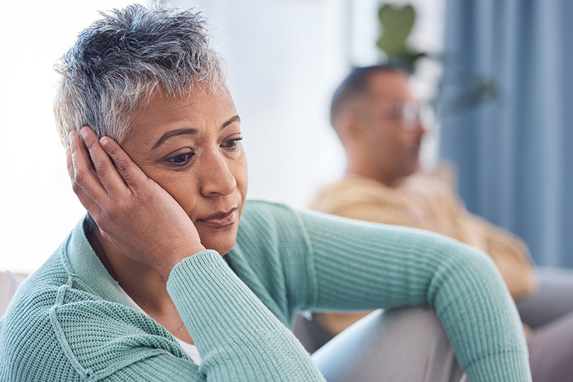 A woman seated on a couch, hand on her chin, considering the body's signals related to anemia and overall well-being.