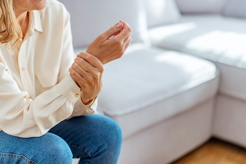 A woman holding her wrist, experiencing joint pain associated with rheumatoid arthritis.