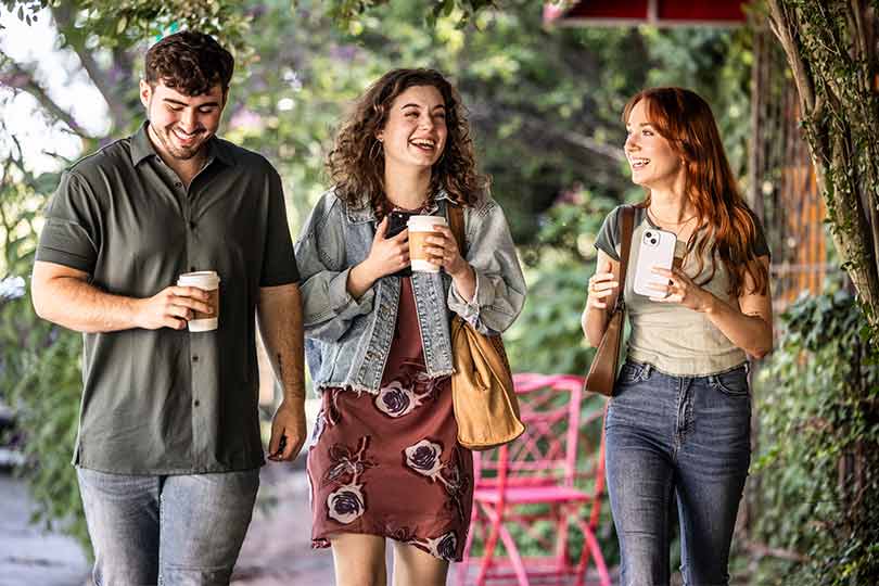One man and two women walking outside together holding coffees, discussing seasonal allergies and tips for allergy season.
