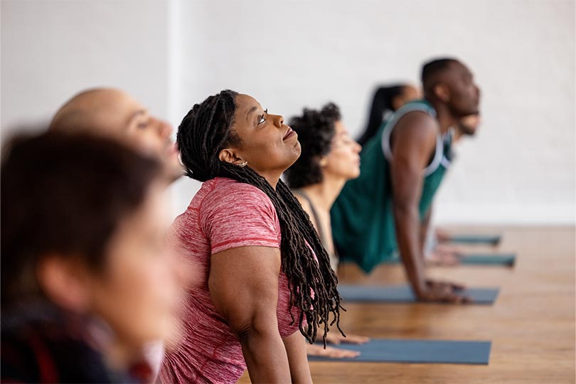 Men and women doing yoga in a workout class to benefit whole health and whole-body wellness.