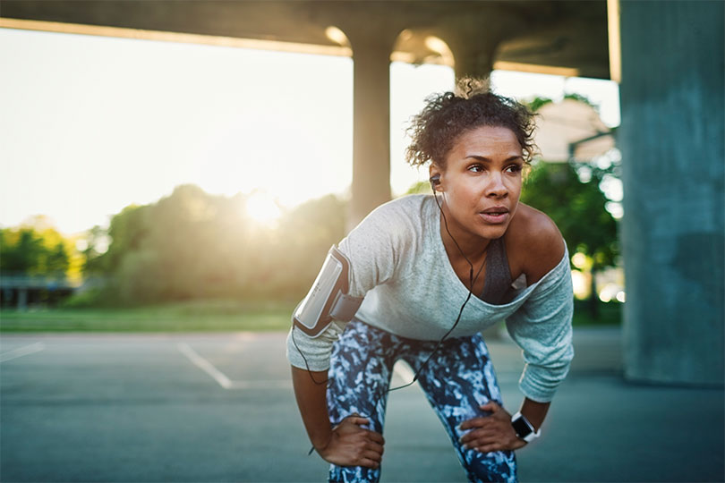 A woman puts her hands on her knees and breathes deeply after a long run