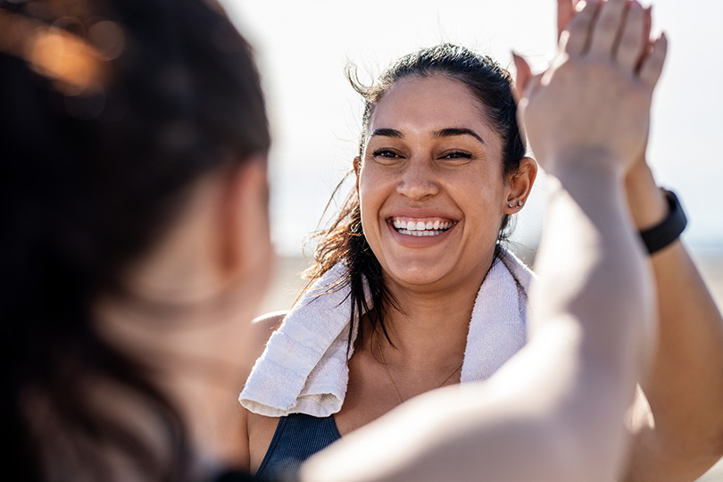 Two women high five on the beach, celebrating wellness through smart health technology and comprehensive health testing.