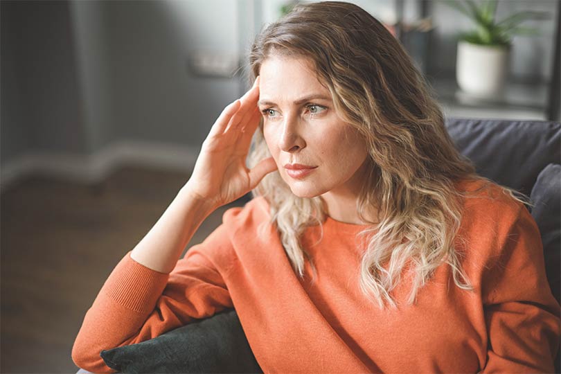 A woman sitting on a couch with her hand on her temple looking stressed, thinking about the connection between stress and cortisol.