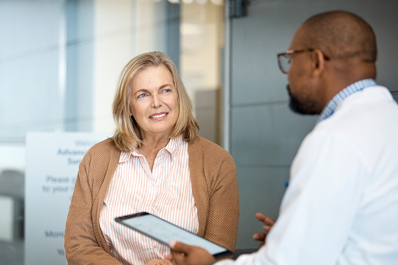 A woman speaks with a doctor in an office, inquiring about Hepatitis B symptoms and the importance of immunity screening.