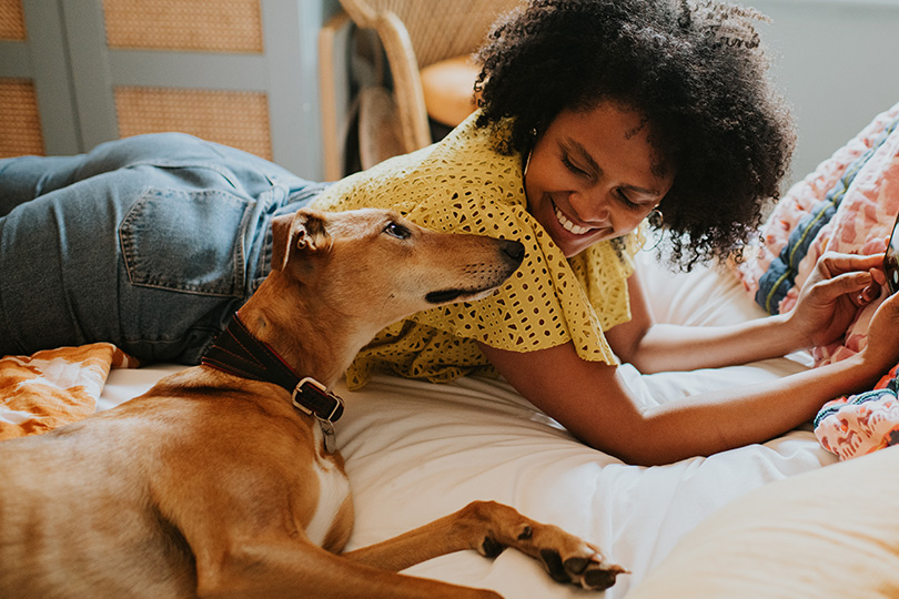 A woman lies on a bed with her dog, both appearing relaxed, illustrating a warm moment of connection and tranquility.