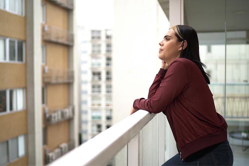 Woman standing outside on a balcony, thinking about the connection between PCOS and high testosterone in women.