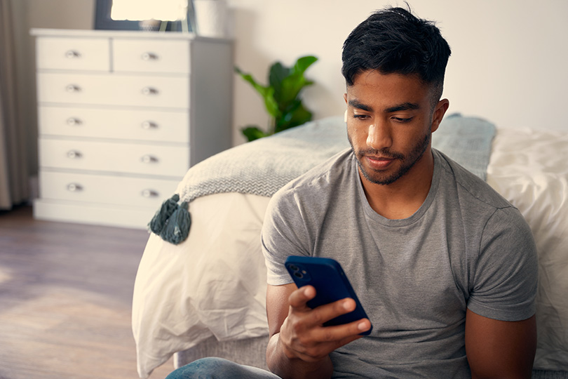 A man sits on the floor, focused on his phone, contemplating food allergies and sensitivities. 