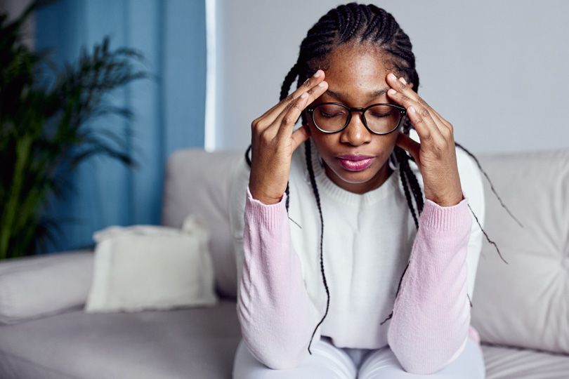 A woman wearing glasses relaxes on a couch, contemplating the four early warning signs of thyroid problems.