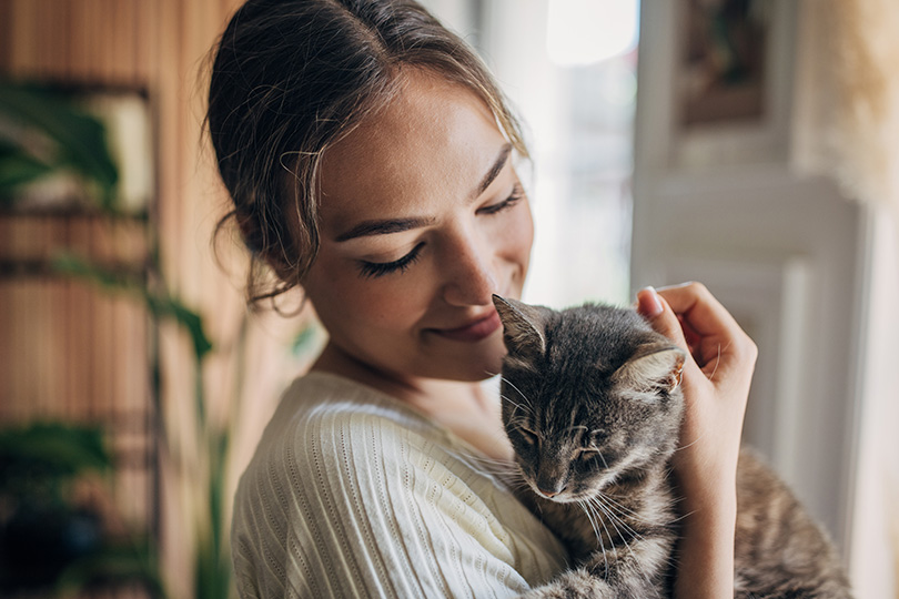 A woman holds a cat in her arms, showcasing a moment of affection amidst cat allergy testing preparations.