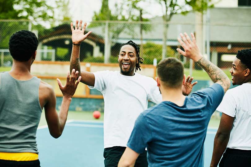 Four men high-fiving each other on a basketball court outside, showing how physical activity can built fitness and community.