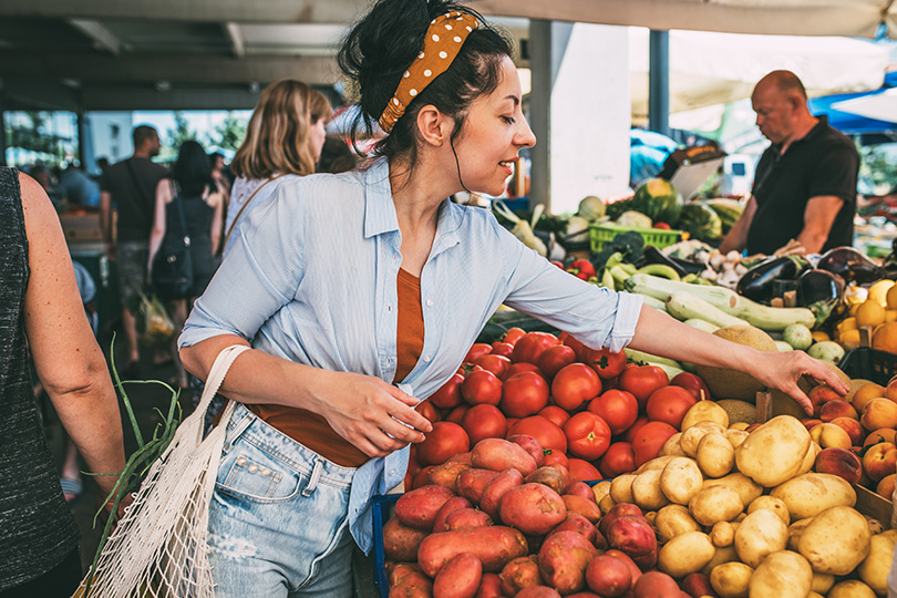 A woman shops for fresh fruits and vegetables at a farmers market, supporting her liver health through nutritious options.