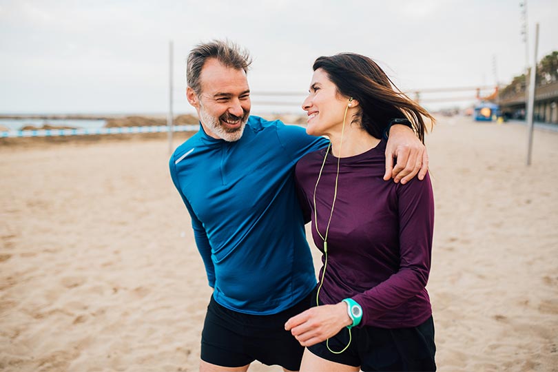 A man and woman share a laugh while being active outdoors on the beach.