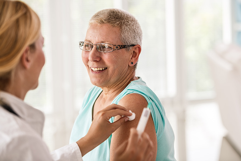 A woman is having her arm checked by a doctor, illustrating the need for regular health assessments and vaccine awareness.