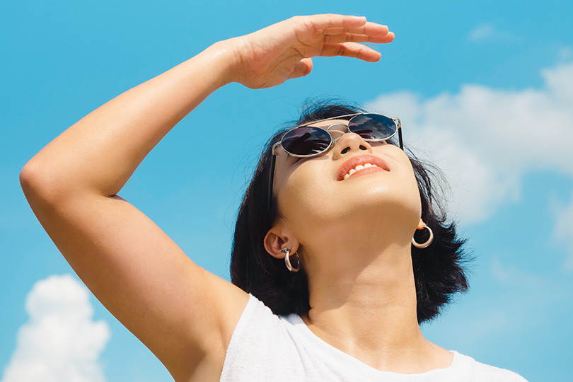 A woman in sunglasses and a white tank top enjoys the sun, highlighting the importance of vitamin D for health.