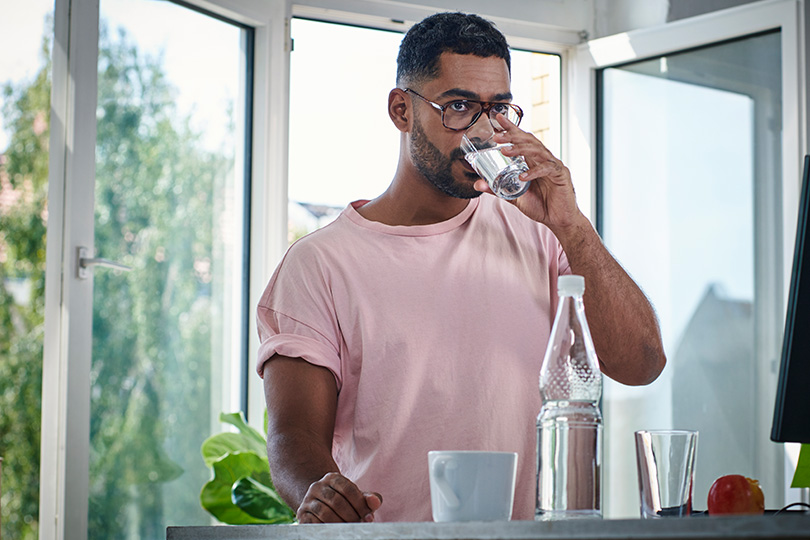 A man in a pink shirt enjoys a refreshing glass of water, promoting hydration while managing diabetes cravings.