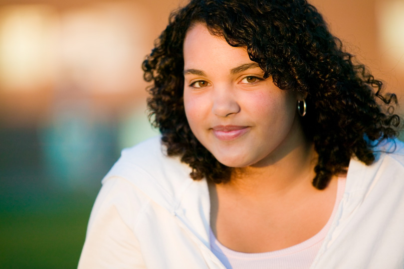 A woman with curly hair wearing a white shirt, representing health awareness related to thyroid conditions.