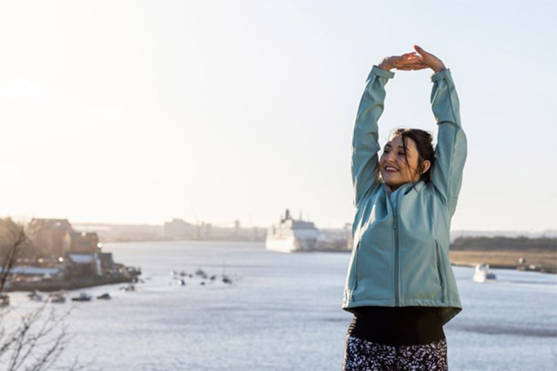A woman stretching by a body of water after doing an outdoor workout to help improve insulin sensitivity and insulin resistance.