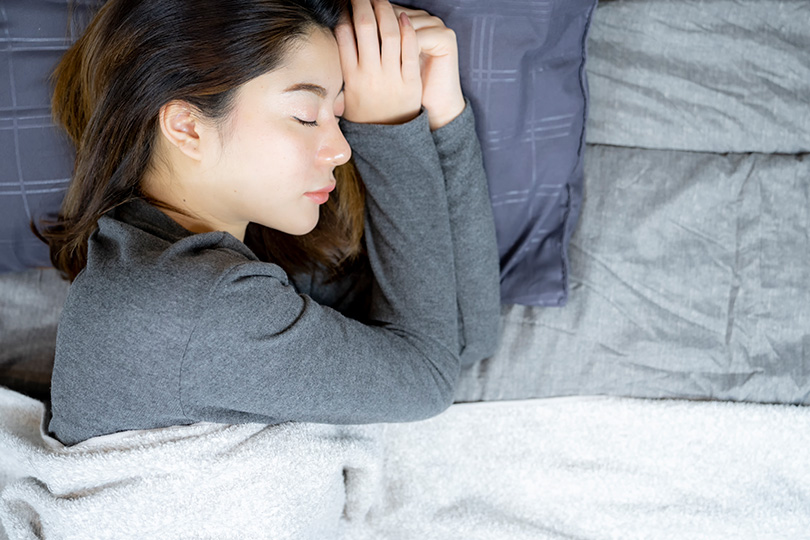A woman in bed, eyes closed in sleep, indicating possible symptoms of chronic fatigue syndrome.