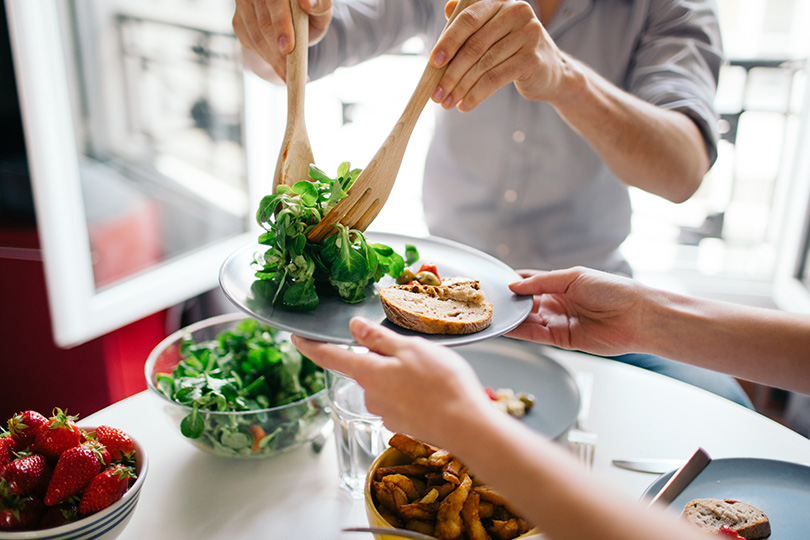 A man joyfully serving a plate of nutritious food, showcasing a healthy lifestyle and positive attitude towards eating.