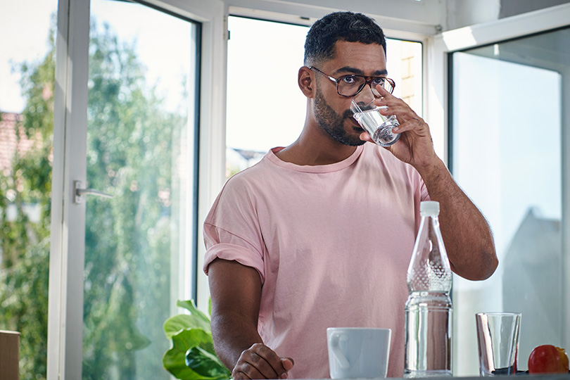 A man in a pink shirt enjoys a refreshing glass of water, promoting hydration while managing diabetes cravings.