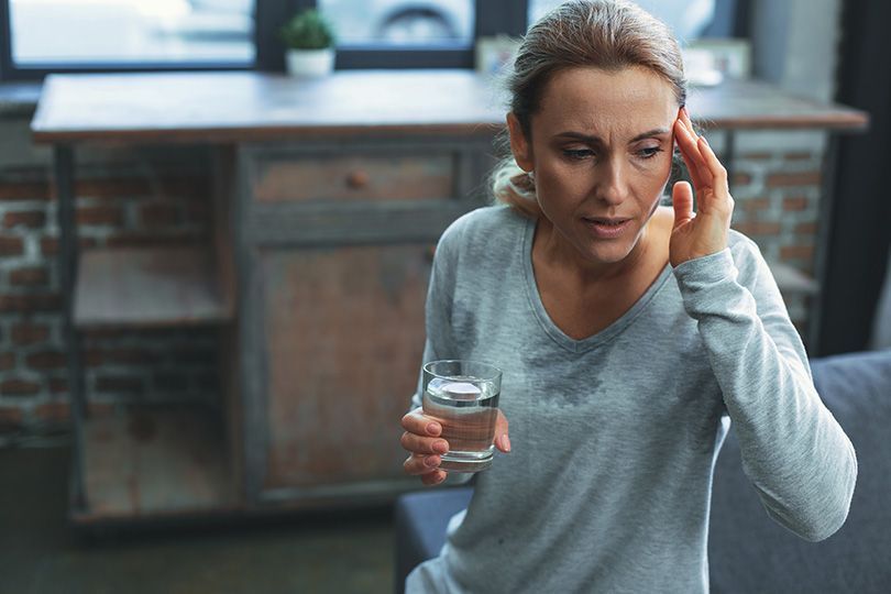 A woman holds a glass of water while looking at her phone, reflecting on menopause myths and facts.