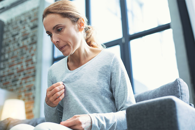 A woman blows breath out of her mouth as she sits on her couch. She is going through menopause and is having a hot flash.