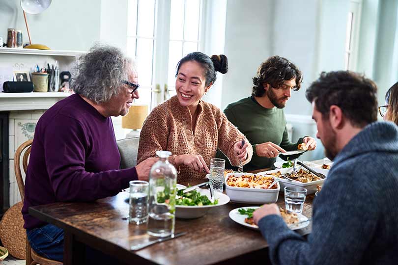 A diverse group of friends sitting around a dining table at home, smiling and sharing a meal together.