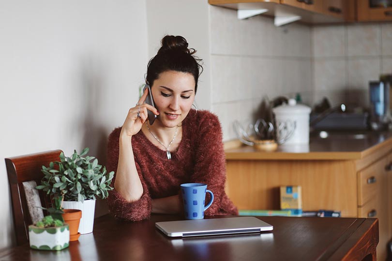 A woman sitting in a kitchen on the phone, speaking with a healthcare provider about pre-pregnancy and preconception testing options.