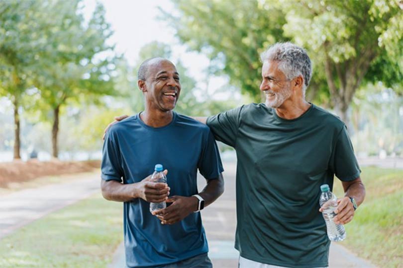 Two men holding water bottles and walking outside together, discussing prostate cancer and the importance of PSA testing.