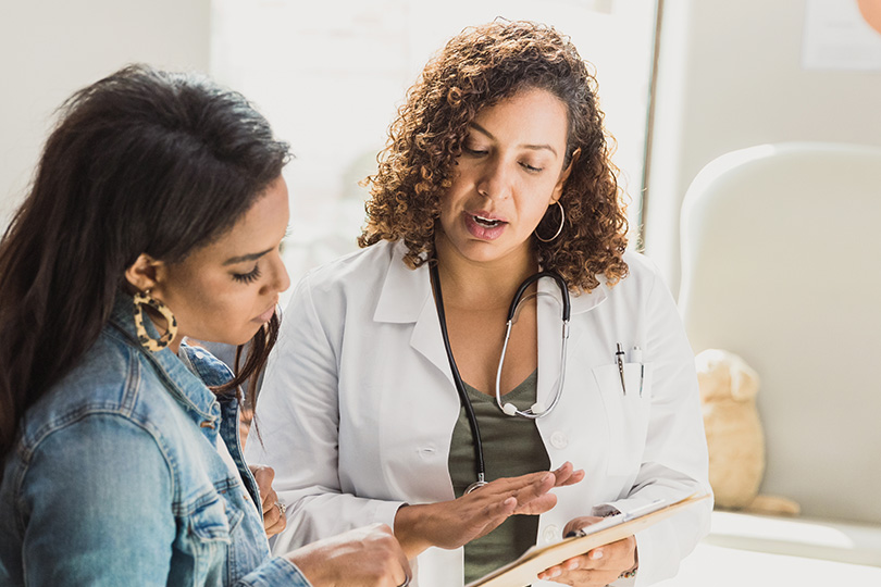 A woman consults a doctor about COVID-19 antibody levels while another woman observes the discussion.