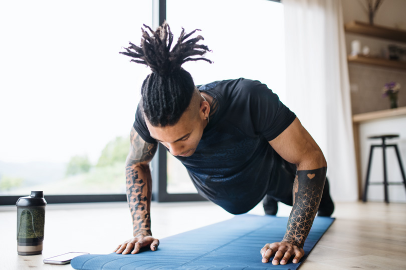A man with dreadlocks does push-ups on a yoga mat, emphasizing the connection between testosterone and fitness goals.