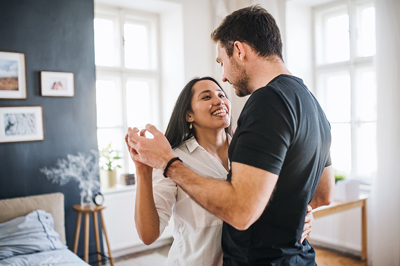 A couple dancing in a warmly lit bedroom, highlighting their bond and the joy of being together in a personal space.