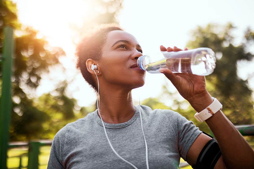 A woman listening to music, going for a run outside, and drinking water, practicing healthy habits for liver health.