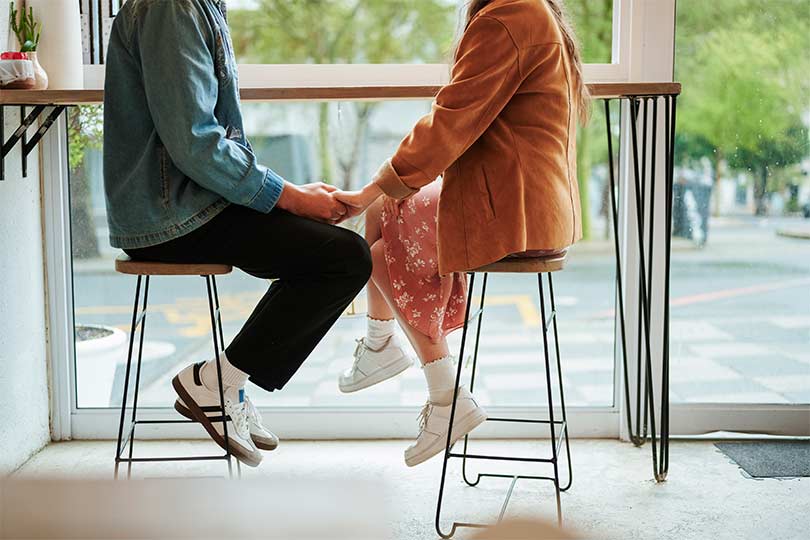 A couple, a man and a woman, sitting together and holding hands, discussing syphilis and other common STIs and the importance of STI testing.