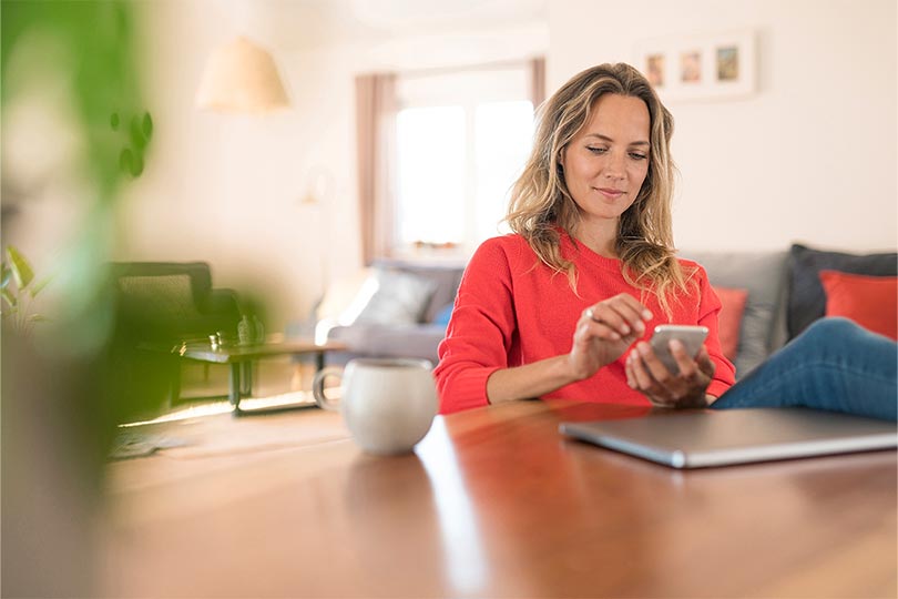 Woman sitting at a table looking at her phone, researching about the role of hormones in PCOS