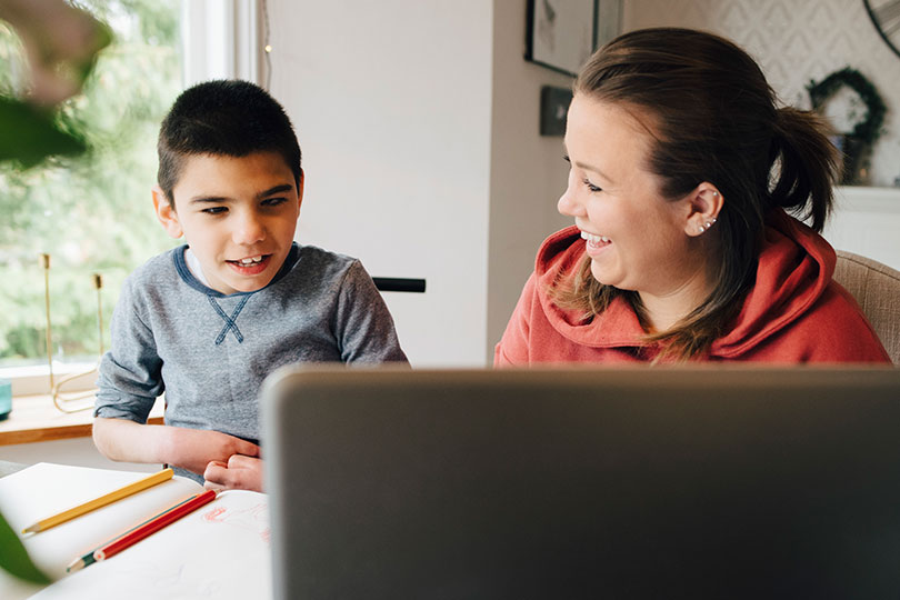 A woman smiles at her son as they work on homework together. She is feeling better after receiving treatment for thyroid issues.