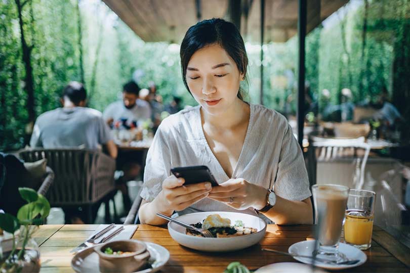 A woman eating alone at a restaurant looking at her phone, looking up what uric acid levels mean for kidney health.