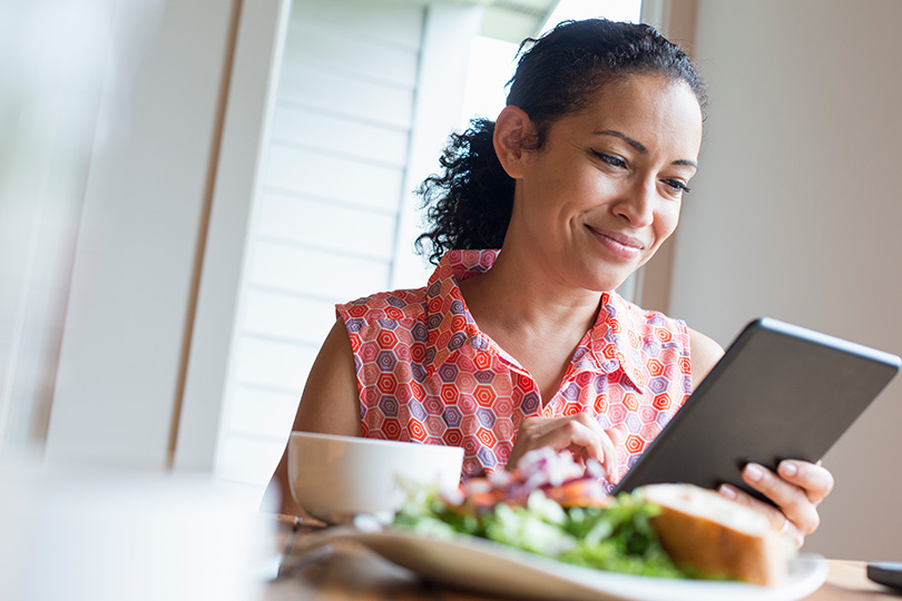 A woman smiles while using a tablet, engaging with information about the four phases of the menstrual cycle.