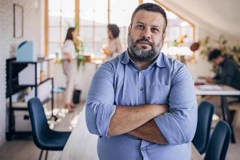 A man stands in an office, exuding professionalism amidst a contemporary workspace filled with natural light.