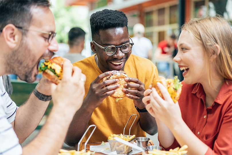 A group of friends eating burgers, which could trigger an immune reaction in people with alpha-gal syndrome or red meat allergy.