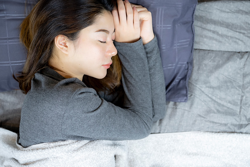 A woman in bed, eyes closed in sleep, indicating possible symptoms of chronic fatigue syndrome.