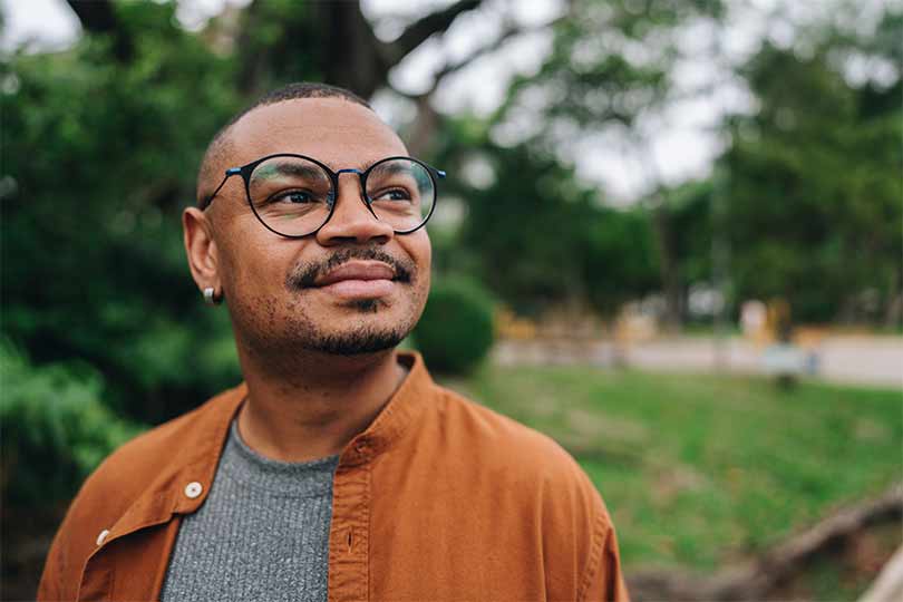 A man wearing glasses standing outside, thinking about what cortisol is and what cortisol levels mean.